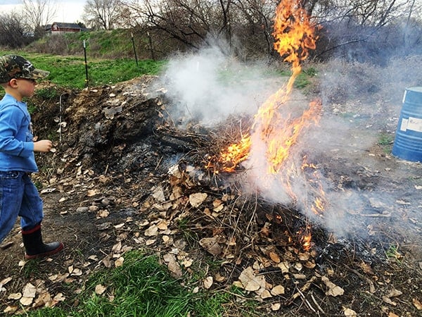A little boy standing by a burn pile. 