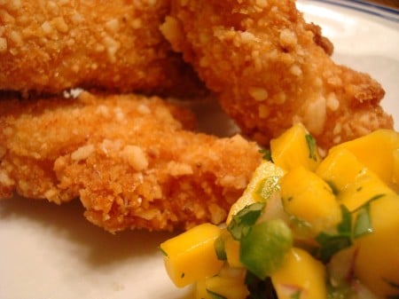 Fried macadamia chicken with mango salsa on a white plate.