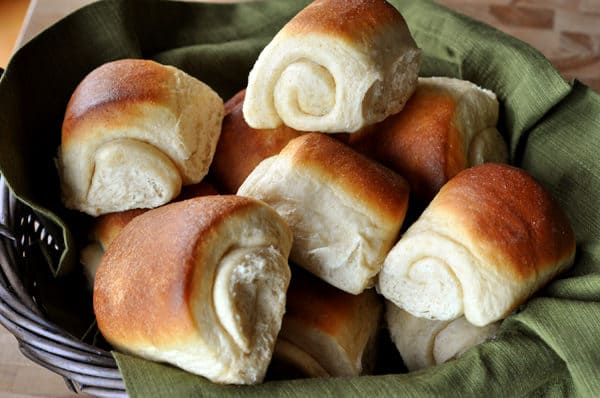 Golden brown rolls on a green napkin in a black basket.