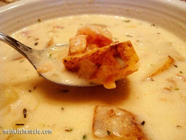 A white bowl of clam chowder with a spoon taking a bite out.