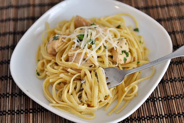 A fork twirling a bite of chicken linguine on a white plate.