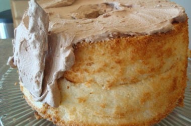 baked angel food cake with chocolate frosting being put on the sides