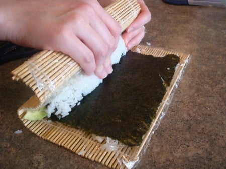 Rolling Roll2 bamboo mat pressing down white rice on a sheet of nori