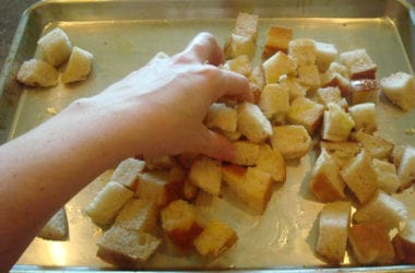 Tossing bread cubes drizzled with oil on a cookie sheet