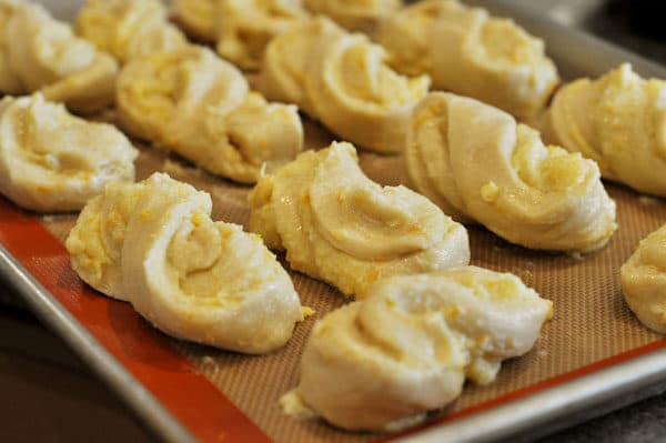 uncooked twisted orange rolls lined up on a sheet pan