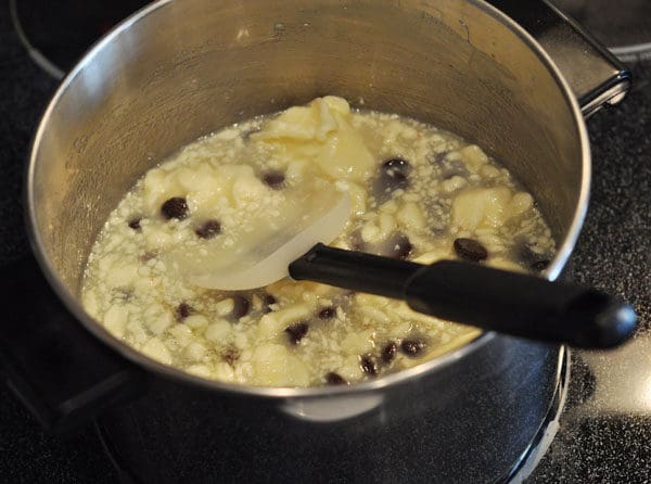 stainless steel pot with caramel ingredients starting to melt and a rubber spatula inside