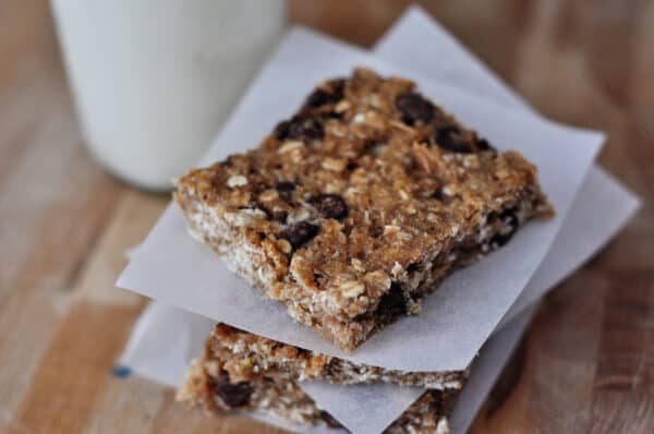 Top view of a square banana oat chocolate chip bar on a piece of parchment paper and stacked on other bars.