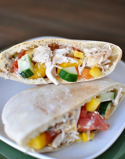 A pita cut in half with an inside view of a greek chicken mixture stuffed inside each pita half.