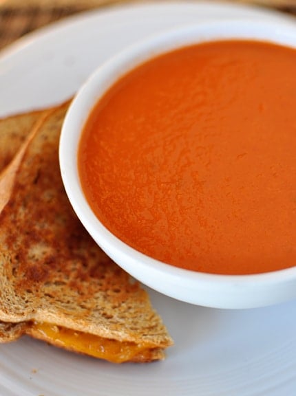 A white bowl of tomato soup with grilled cheese on the side.
