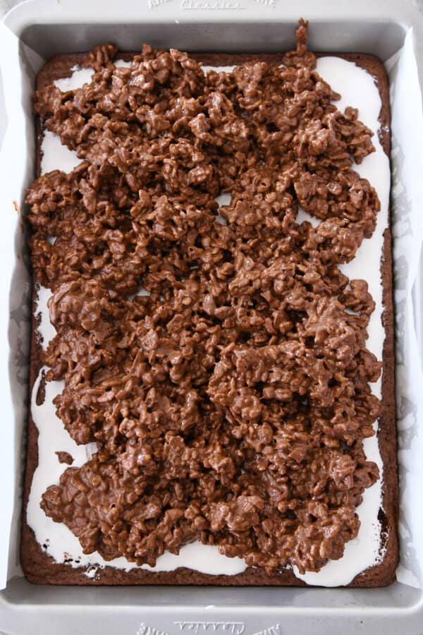 Spreading crispy peanut butter chocolate topping on top of marshmallow cream on brownies.