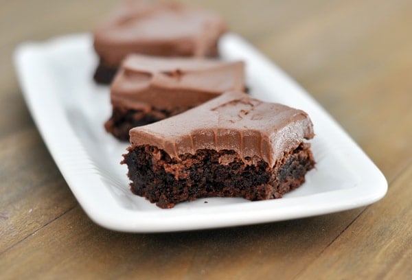 Three chocolate frosted brownies, one with a bite taken out, on a white platter.