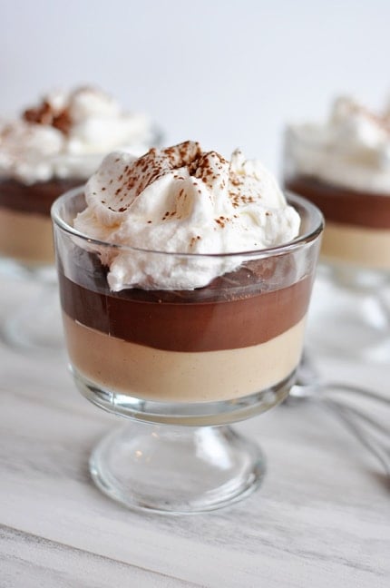 A glass goblet with a layer of peanut butter pudding topped with a layer of chocolate pudding and whipped cream.