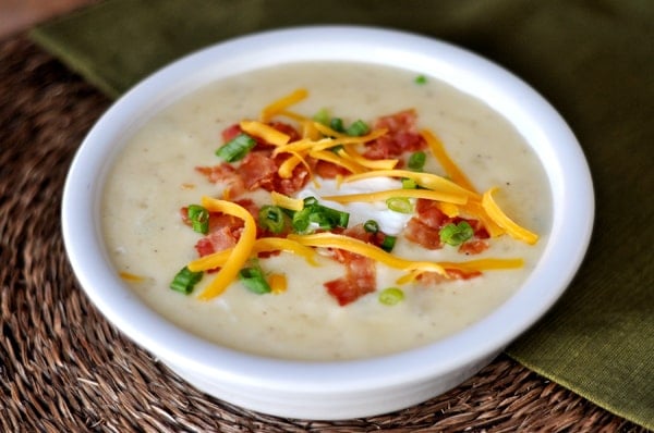 a white bowls off creamy potato soup sprinkled with cheese, green onions, and bacon. 