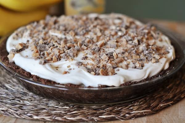 A chocolate cookie crust banana pie with whipped cream and chopped toffee on top.