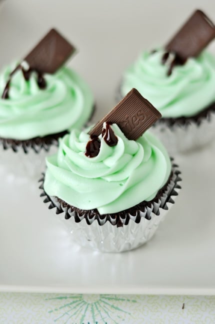 Chocolate cupcake in a metallic liner with light green piped frosting and an Ande's mint standing tilted in the frosting.