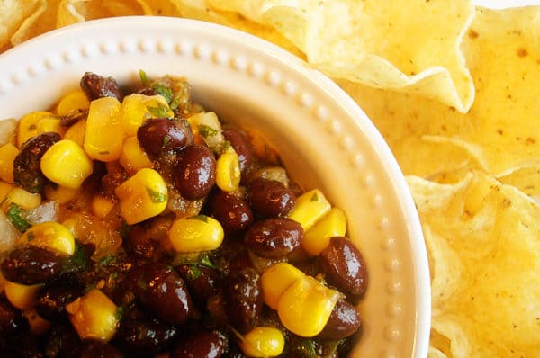 Black bean and corn salsa in a white bowl next to tortilla chips.