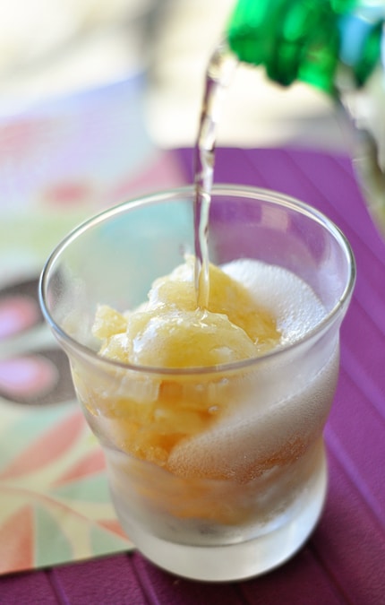 A glass full of slush with pop being poured into the glass.