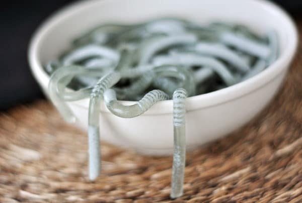 A white bowl filled with Jello worms and a few hanging off the sides.