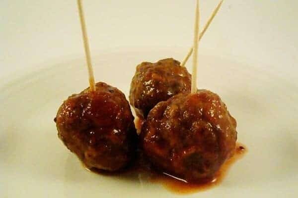 Three saucy meatballs with toothpicks in them on a white plate.