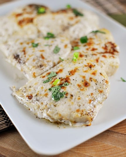 Top view of cooked chicken with melted cheese lined up on a white platter.