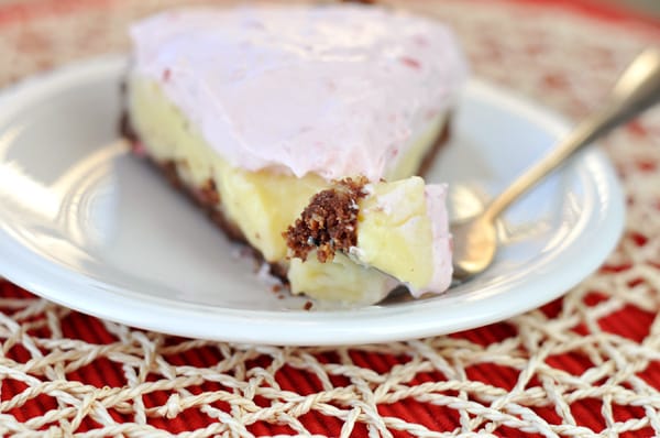 A piece of banana split pie with a bite taken out on a white plate.