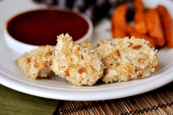 A white plate with homemade chicken nuggets in front of a white bowl of sauce.