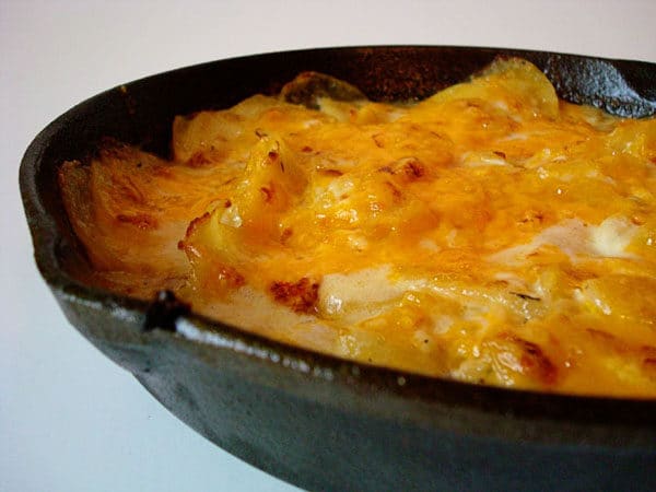 Cast iron skillet with scalloped potato and melted cheese.