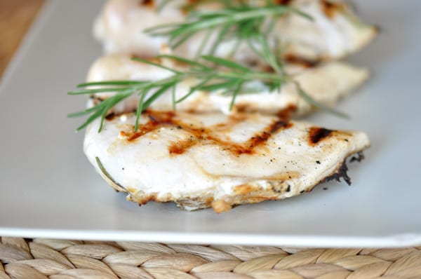 Grilled chicken breasts on a white platter with sprigs of fresh rosemary on top.
