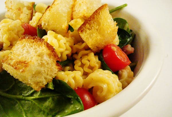 White bowl with tomatoes, pasta, spinach, and croutons.