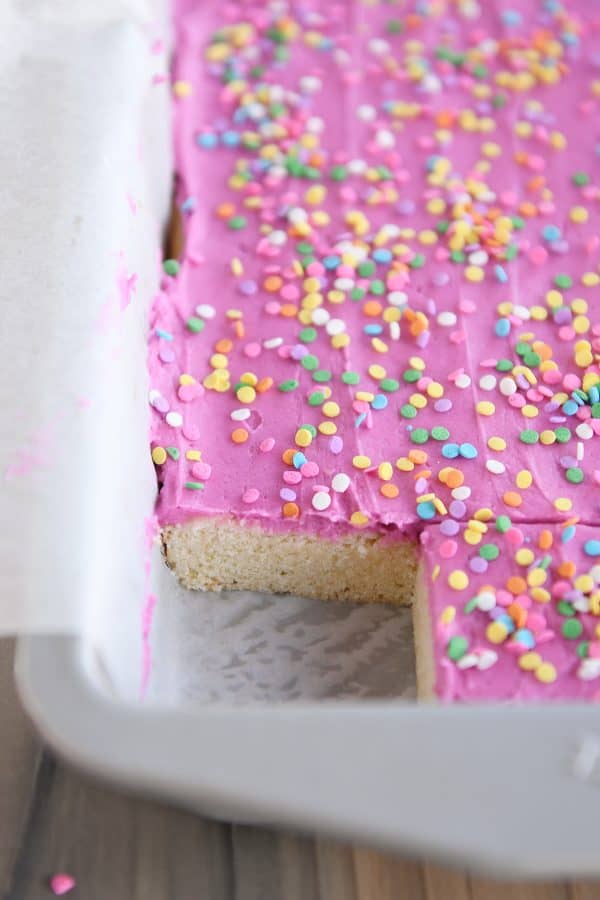 Pan of frosting-covered sugar cookie bars with one bar cut out in the corner.