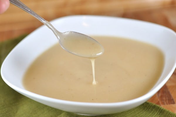 white bowl full of light colored turkey gravy, with a spoon taking some out