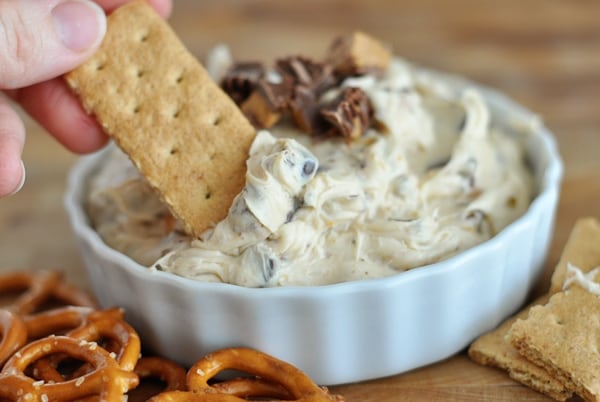 A white bowl full of peanut butter cookie dough dip with a graham cracker dipped in it.