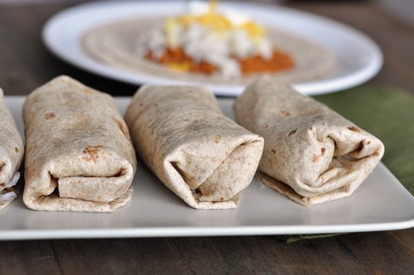 Burritos lined up in a row on a white platter.