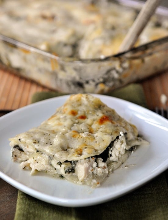 White plate with a piece of chicken and spinach lasagna in front of the rest of the casserole.