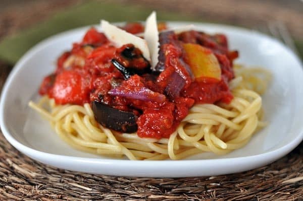 White plate with cooked spaghetti noodles topped with a chunky red sauce.