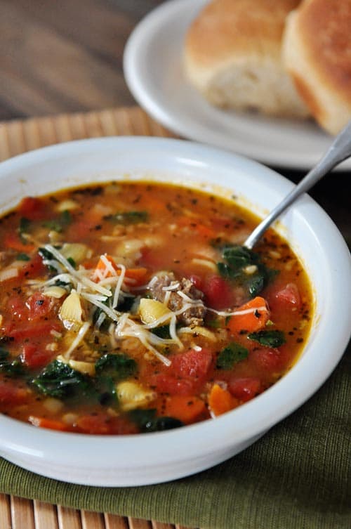 White bowl full of Tuscan sausage soup full of pasta, spinach, and tomatoes. 