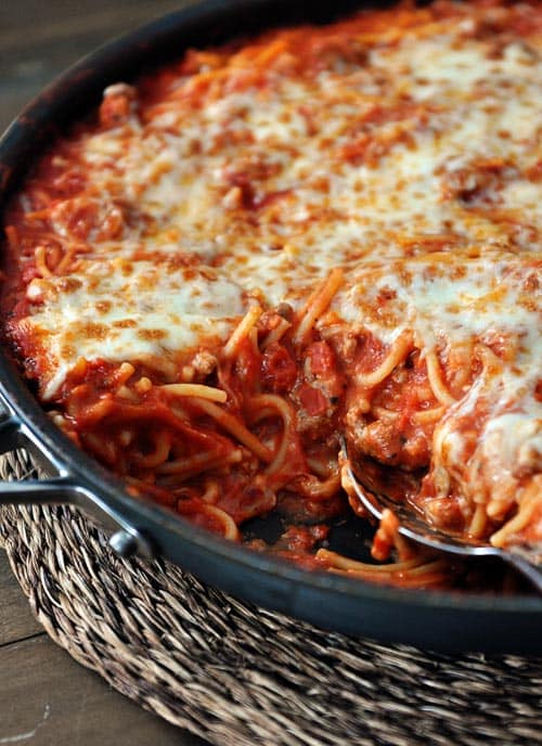 A cast iron skillet full of cheese-topped spaghetti.