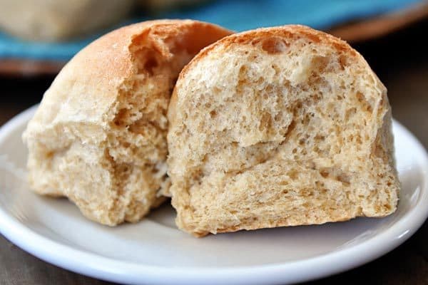 A whole wheat roll split in half on a white plate.