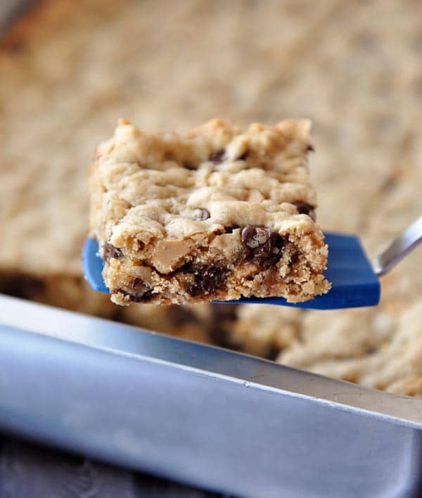 A small blue spatula holding a chocolate chip peanut butter oatmeal bar over a pan of the rest of the bars.