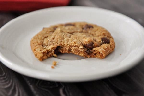 A white plate with a chocolate chip cookie with a bite taken out.