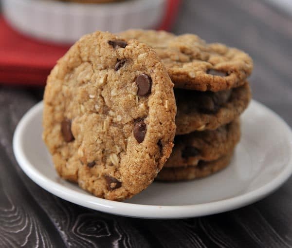 A white plate with stacked chocolate chip cookies and one laying on it's side on the stack.