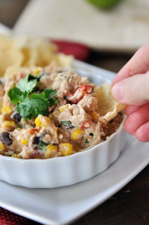 A tortilla chip being dipped into a white ramekin full of a creamy tex-mex mixture.