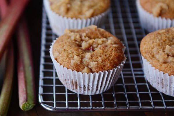 Streusel-topped rhubarb muffins on a cooling rack next to fresh rhubarb.
