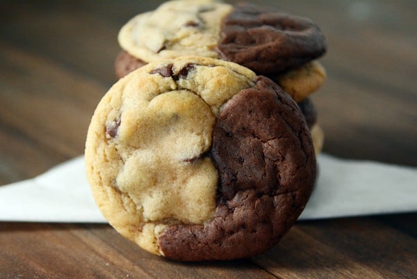A stack of half brownie, half chocolate chip cookie cookies with one cookie leaning on the stack..