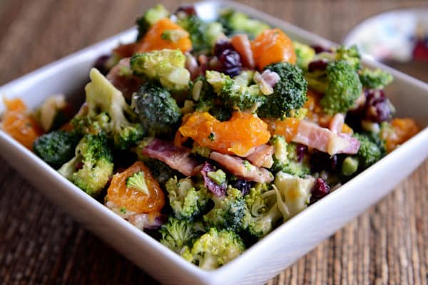 A bowl full of a mandarin, broccoli, bacon, and craisin salad. 