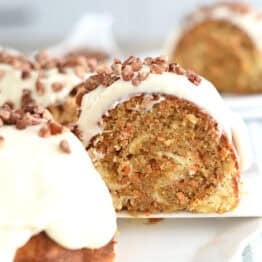 A slice of carrot and cream cheese swirled bundt cake being taken off a white plate with a white spatula.