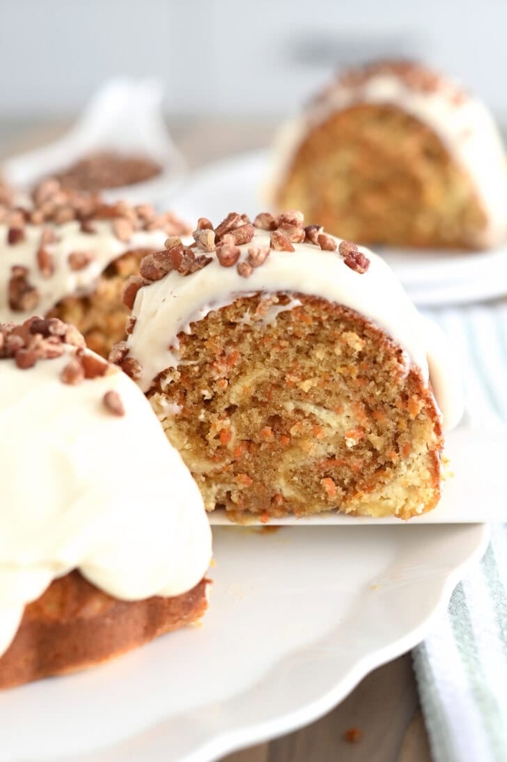 A slice of carrot and cream cheese swirled bundt cake being taken off a white plate with a white spatula.