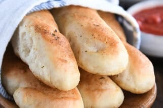 Stack of homemade breadsticks on wooden tray.