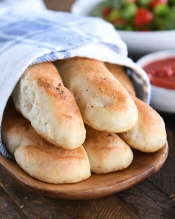 Stack of homemade breadsticks on wooden tray.