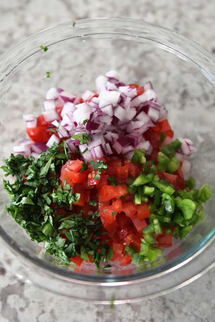 Glass bowl with cilantro, tomatoes, jalapenos and red onion.